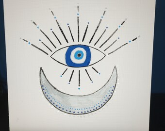 Puede incluir: Un lienzo blanco con un ojo azul maligno y una luna creciente plateada pintados en él. El ojo maligno tiene una pupila negra y un anillo blanco alrededor. La luna creciente tiene un contorno plateado y está llena de un color gris claro. El ojo maligno y la luna creciente están rodeados de líneas negras con puntos azules.