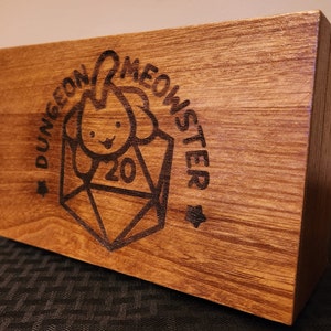 May include: A wooden box with a Dungeons & Monsters logo featuring a cartoon dog and a 20-sided die.