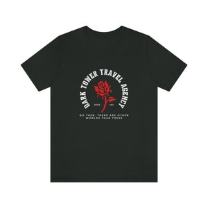 Puede incluir: Camiseta negra con un gr&aacute;fico circular blanco que presenta una rosa roja y el texto "Dark Tower Travel Agency Since 1982" y "Go then, there are other worlds than these."