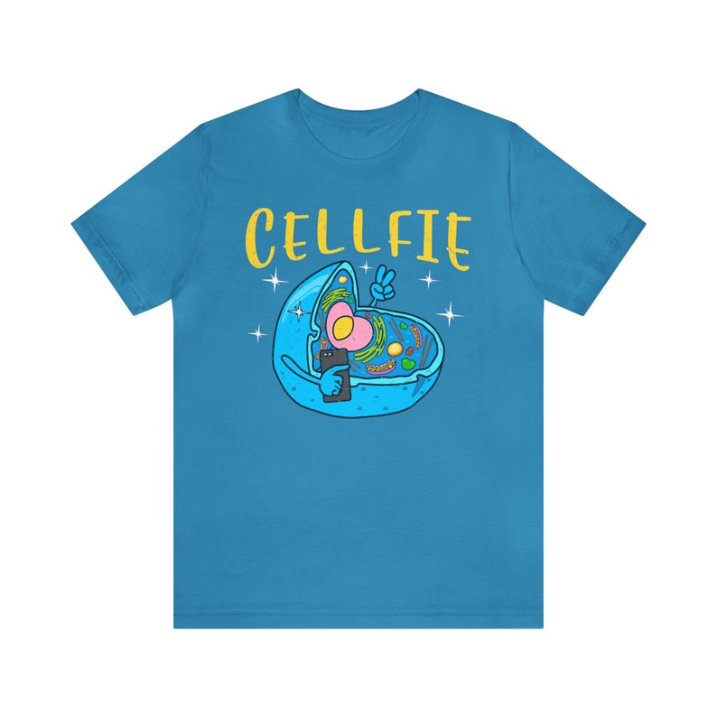 May include: A turquoise t-shirt with a cartoon cell design. The cell, in blue, is taking a selfie with a smartphone. The word "CELLFIE" is written in yellow above the cell, with a peace sign. The cell has a pink nucleus.