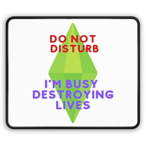 Puede incluir: Alfombrilla de ratón rectangular blanca con borde negro. La alfombrilla presenta el texto "DO NOT DISTURB" en rojo sobre una forma de diamante verde. Debajo, el texto "I'M BUSY DESTROYING LIVES" está en morado.