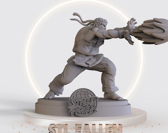 May include: A gray 3D printed figurine of a character from Street Fighter, Ryu, in a fighting pose with a fireball effect. The figurine is on a base with the Street Fighter logo. The text "STL FALLEN" is below the base.