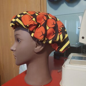 May include: A black and yellow striped satin bonnet with red boxing glove print. The bonnet is on a mannequin head.