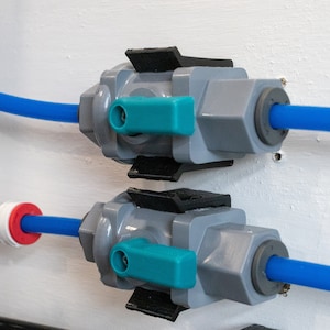 May include: Two gray plastic water valves with blue and teal handles are mounted on a white wall. Each valve has a blue hose attached to it.