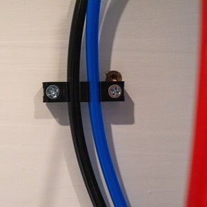May include: Close-up of three cables secured to a white wall with black plastic clips. The cables are black, blue, and red.