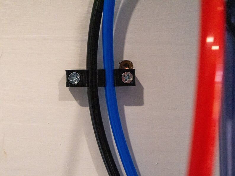 May include: Close-up of three cables secured to a white wall with black plastic clips. The cables are black, blue, and red.