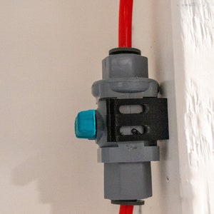 May include: A gray plastic water filter with a blue lever and a red hose attached to it. The filter is mounted on a white wall.