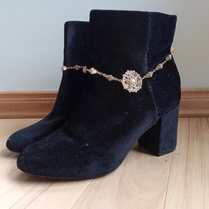 May include: Black velvet ankle boots with a gold chain and a large rhinestone embellishment.