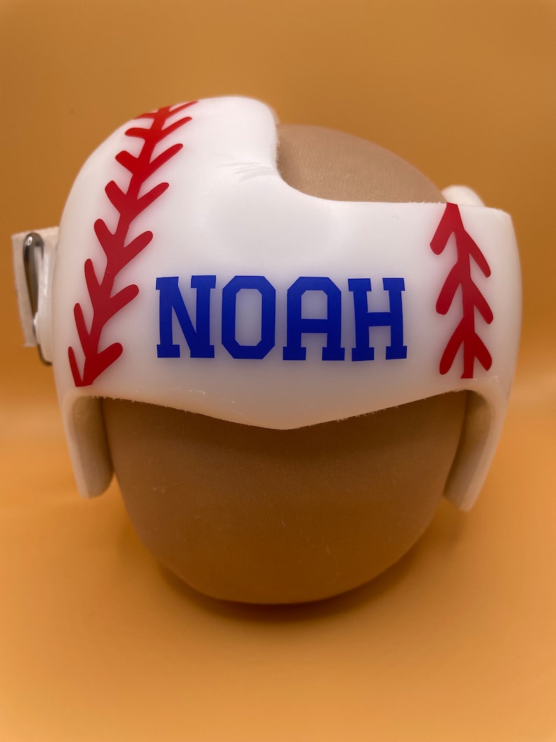 May include: White baseball helmet with red stitching and a blue name 'NOAH' on the front.