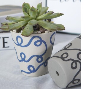 May include: Two ceramic plant pots with a white background and a blue and black abstract design. The pot on the left has a succulent plant growing in it.