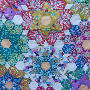 May include: A colourful quilt made of hexagonal fabric patches. The quilt features a repeating pattern of stars and flowers in shades of blue, green, pink, and yellow.