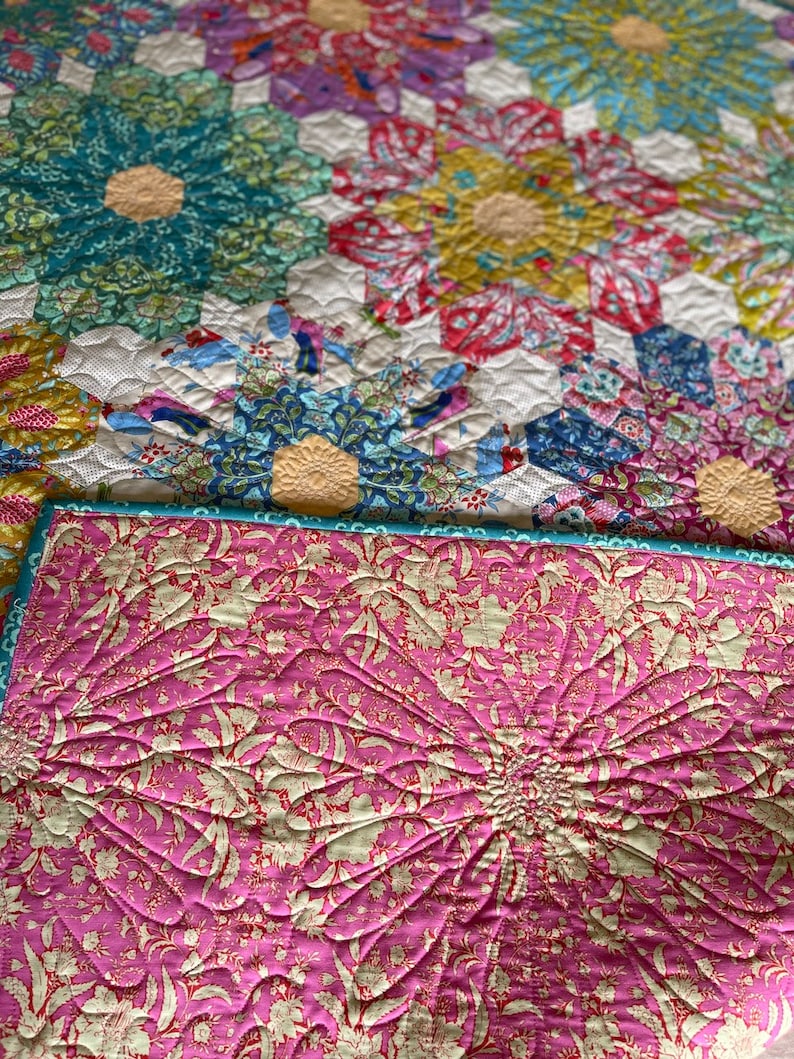 May include: A pink quilt with a floral pattern and a quilted design. The quilt is folded in half and the back side is visible.