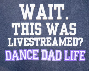 May include: A dark blue t-shirt with white text that reads "WAIT. THIS WAS LIVESTREAMED? DANCE DAD LIFE". The words "DANCE DAD LIFE" are in a purple outline.