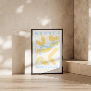 Może przedstawiać: Czarny plakat w ramie z białym tłem i abstrakcyjnym wzorem w kolorze ż&oacute;łtym i niebieskim przedstawiającym tor wyścigowy Grand Prix Monako 2024. Plakat zawiera tekst "MONACO" i "GRAND PRIX 2024" w kolorze czarnym.