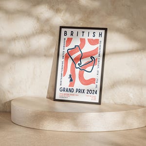 May include: A poster with a black frame advertising the British Grand Prix 2024. The poster features a stylized map of the Silverstone Circuit in red and blue on a white background. The text on the poster reads "BRITISH GRAND PRIX 2024" and "SILVERSTONE CIRCUIT, STH - 7TH JUL".