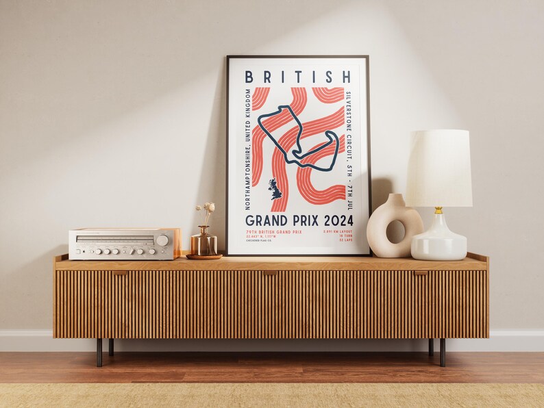 May include: A poster with a minimalist design featuring a red and white track map for the British Grand Prix 2024. The poster is framed in black and is displayed on a wooden shelf with a vintage stereo and a lamp.