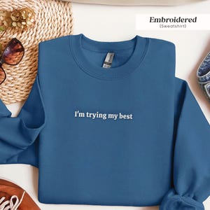 May include: A blue sweatshirt with the text "I'm trying my best" embroidered in white on the front.