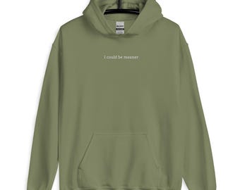 Pode incluir: Uma jaqueta de moletom verde com capuz, com um bolso branco e o texto "I could be meaner" impresso na frente.