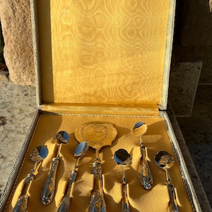 May include: A set of silver-plated serving utensils in a yellow velvet-lined box. The set includes a cake server, a spoon, and six small spoons.