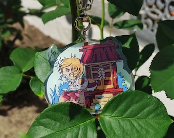 May include: A clear acrylic charm with a cartoon illustration of a blonde character with a cat in front of a red and white shrine. The charm is attached to a silver chain.