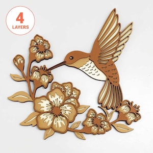 May include: A layered wooden hummingbird wall art piece with a brown and white color scheme. The hummingbird is depicted with outstretched wings, hovering near flowers. The text "4 LAYERS" is in a circle in the upper left corner.