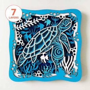 May include: A layered paper art piece featuring a sea turtle design. The artwork uses shades of blue and white to depict the turtle, aquatic plants, and fish. The frame is a bright blue, and the piece has seven layers.