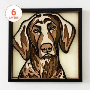 May include: A framed, layered wooden artwork depicting a dog's face. The piece uses various shades of brown, beige, and white. The frame is black. The text "6 LAYERS" is in a circle in the upper left corner. The dog's face is the focal point.