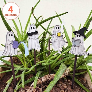 May include: Four ghost-shaped plant stakes featuring different activities: one watering with a purple can, one holding a black cat, one drinking from a yellow mug, and one wearing a black witch hat while reading a book. Each stake has a brown stick.