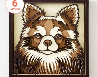 Op de afbeelding: Een meerlagig houten kunstwerk dat het gezicht van een hond afbeeldt, in tinten bruin en crème. Het kunstwerk is geplaatst in een donkerbruine vierkante lijst. De tekst "6 LAYERS" staat in een cirkel linksboven.
