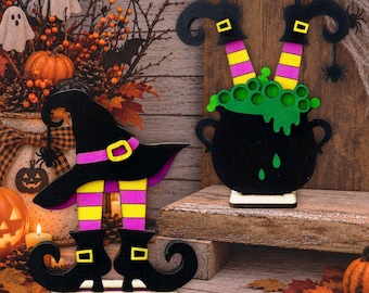 May include: Two wooden Halloween decorations featuring witch legs. One shows a black witch hat with purple and yellow striped legs and black boots. The other shows a black cauldron with green bubbling liquid and purple and yellow striped legs.