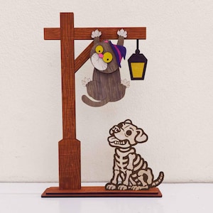 May include: A wooden decorative display featuring a brown post with a hanging lantern and a grey cat with yellow eyes and a purple hat clinging to the crossbar. Below the cat sits a light brown dog figure with a visible white skeleton print.