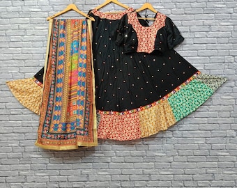 May include: A black, embroidered Indian outfit with a matching scarf. The outfit includes a short-sleeved top and a long skirt with colorful patchwork. The scarf features a vibrant mix of colors and patterns, with gold trim.