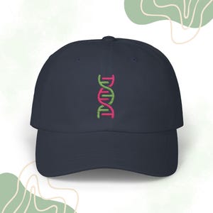 Op de afbeelding: Een donkerblauwe baseballpet met een geborduurd roze en groen DNA-dubbelhelix op de voorkant.