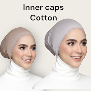 May include: Two cotton inner caps, one in a light brown colour and the other in a light grey colour. The caps are made of a soft, stretchy fabric and are designed to be worn under a hijab.