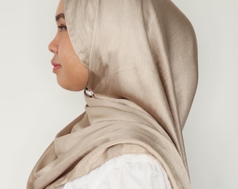May include: A light brown satin hijab with a subtle striped pattern. The hijab is draped over the head and shoulders.