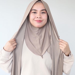 Op de afbeelding: Een vrouw draagt een lichtbruine hijab met een losse, vloeiende stijl. De hijab is gemaakt van een zachte, rekbare stof en is ontworpen om comfortabel en gemakkelijk te dragen.