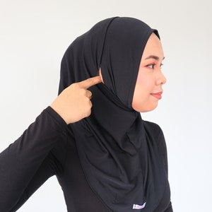 May include: A black long-sleeved shirt with a mock neck and a black hijab. The person is wearing blue jeans.