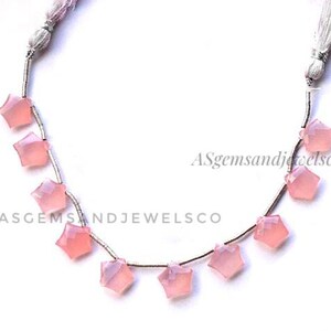 Può includere: Una collana di perle a forma di stella in calcedonio rosa su un filo d'argento. Le perle sono infilate su un filo d'argento e hanno un aspetto naturale, leggermente traslucido. Le perle misurano circa 10 mm. Agemsandjewelsco è stampato sullo sfondo bianco.