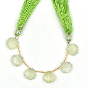 May include: A strand of light green gemstone beads in a shell shape, strung on a gold chain with green tassel ends.