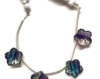 May include: A strand of silver beads with four faceted flower-shaped beads. The beads are a mix of purple, blue, and green.
