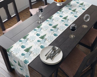 Puede incluir: Un camino de mesa blanco con un patrón repetido de muñecos de nieve y copos de nieve. El camino de mesa está sobre una mesa de madera oscura con dos copas de vino y un plato de cubiertos.