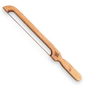May include: A wooden bread slicer with a stainless steel wire. The handle is made of light brown wood and features the text "Think4Earth". The wire is stretched across a rectangular opening in the wooden frame.