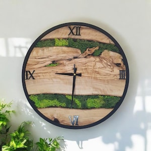 May include: A round wooden clock with Roman numeral markings and a black frame. The clock face is decorated with green moss and wood.