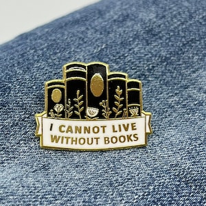 May include: Gold enamel pin featuring a stack of black books and a white banner that reads "I cannot live without books".