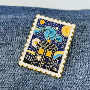May include: A gold-coloured enamel pin featuring a blue and white TARDIS with the words "POLICE BOX" on the side, set against a starry night sky reminiscent of Vincent van Gogh's "Starry Night" painting. The pin is shaped like a postage stamp with a white border and gold edging.