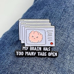 May include: A white enamel pin featuring a cartoon brain inside a computer window with multiple tabs open. The text below reads "My brain has too many tabs open."