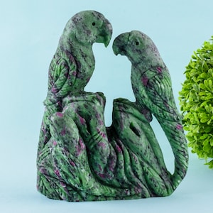 Può includere: Una scultura in pietra verde e rosa di due pappagalli appollaiati su un ramo. La scultura è realizzata in una varietà di pietra preziosa chiamata zoisite rubino.