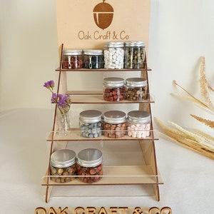 May include: A wooden display stand with four shelves, showcasing various colours of sealing wax in glass jars. The stand has a sign at the top that reads "Oak Craft & Co." and a smaller sign at the bottom that reads "OAK CRAFT & CO."