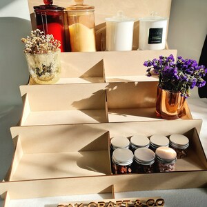 May include: A wooden tiered display stand with a sign that reads "OAK-CRAFT & CO". The stand is filled with various items, including candles, jars, and small containers.