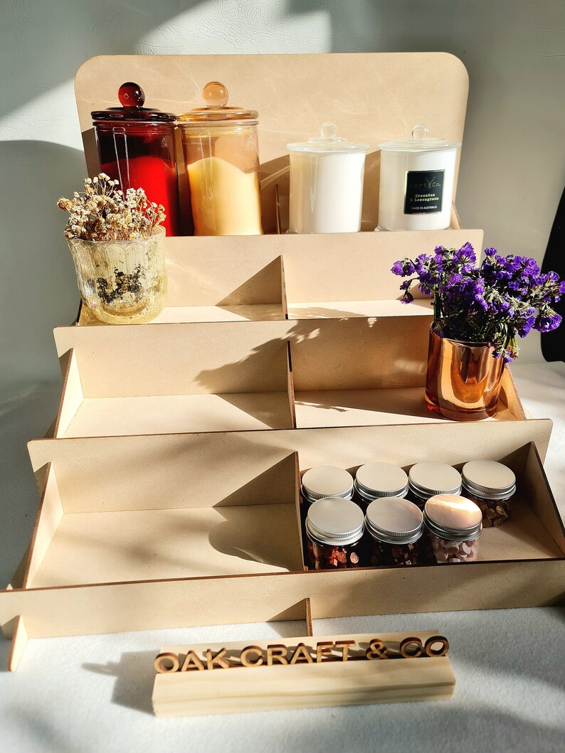 May include: A wooden tiered display stand with a sign that reads "OAK-CRAFT & CO". The stand is filled with various items, including candles, jars, and small containers.